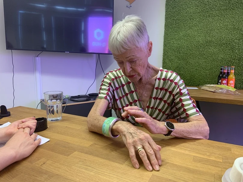 Eine Frau sitz an einem Tisch und schaut sich die Uhr an ihrem Handgelenk an und drückt auf die Uhr.